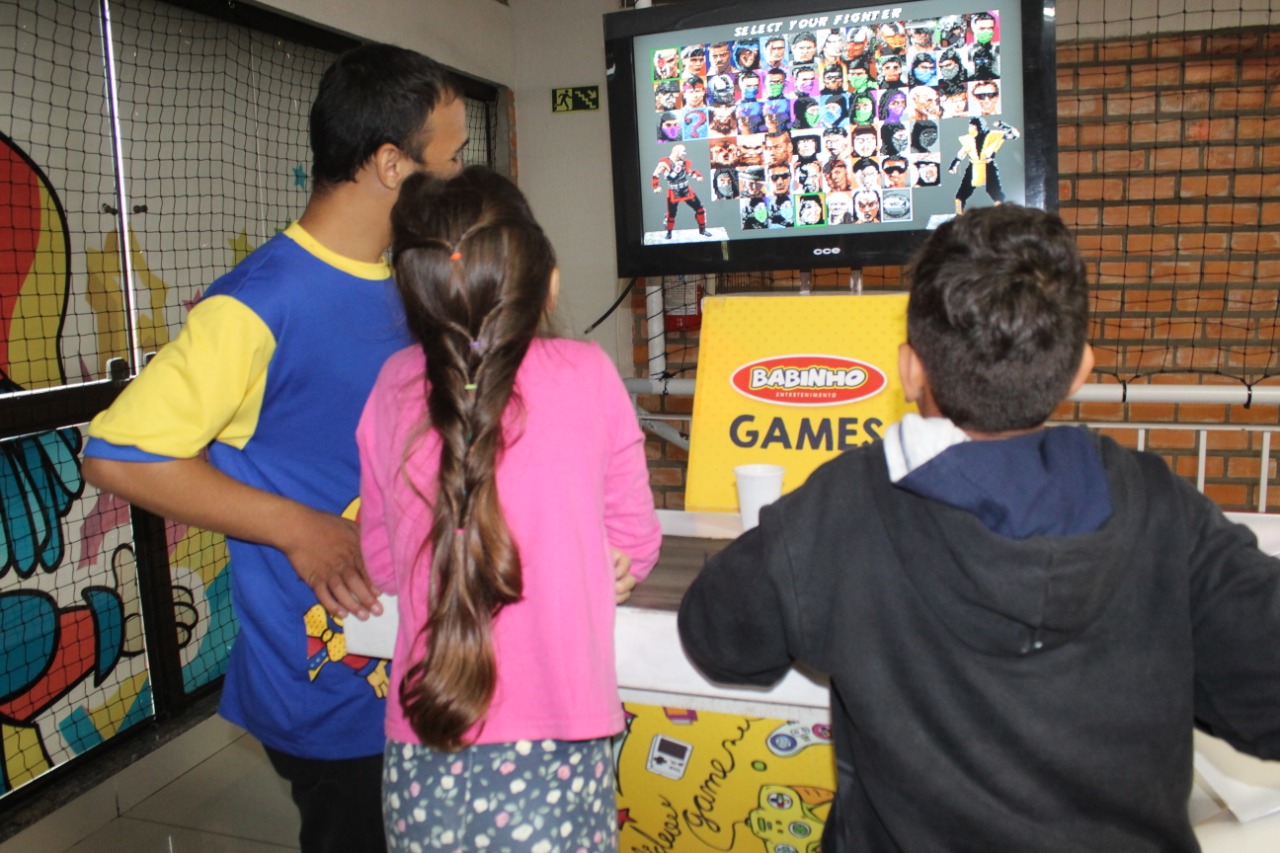 Dois meninos e uma menina, associados da ADEVIC, se divertem em frente ao videogame